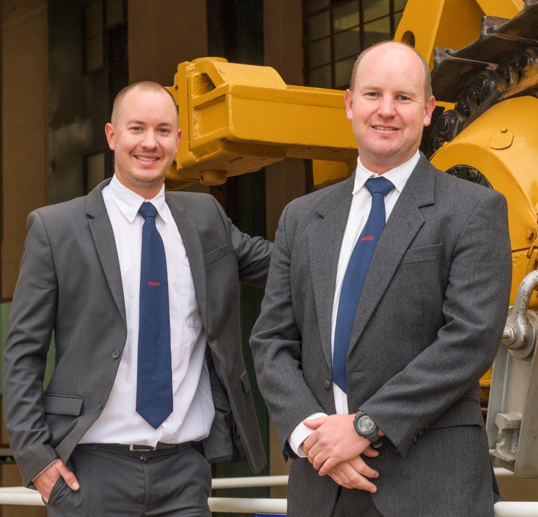 Two men in suits standing in front of a yellow construction vehicle
AI-generated content may be incorrect.